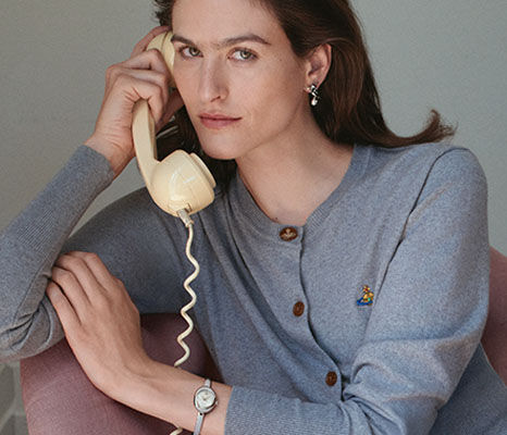Woman in a grey cardigan holding a vintage telephone and wearing a silver watch.